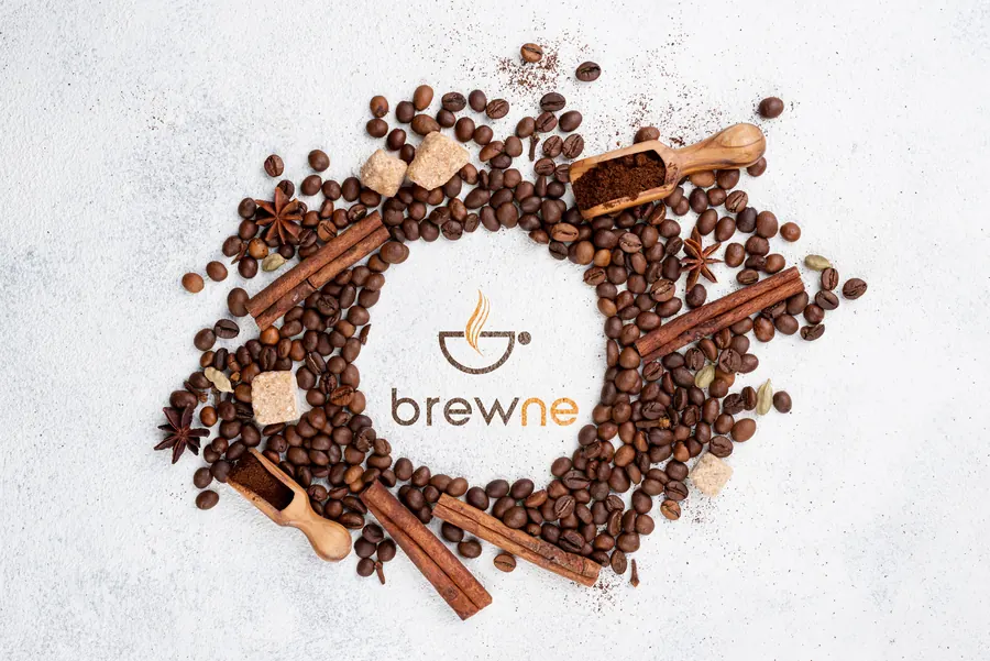 Roasted coffee beans, cinnamon and wooden scoops arranged in a ring around the Brewne logo