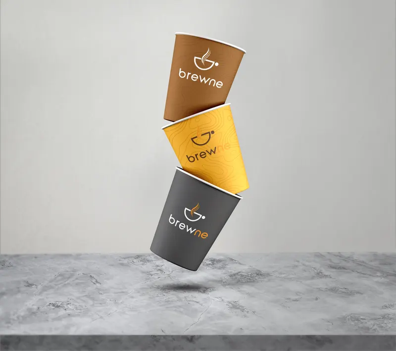 Three Brewne takeaway cups in brown, orange and charcoal, stacked mid-air